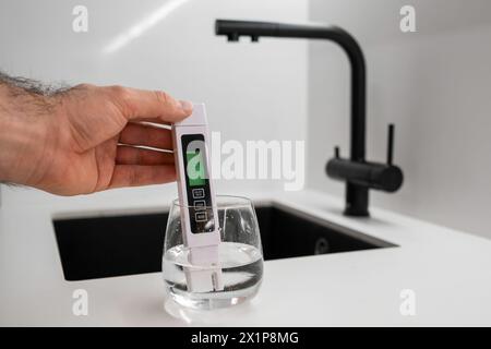 Man Hand immerge il tester TDS o il conduttometro nell'acqua in vetro. dimostra che l'acqua è pulita. Foto Stock