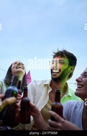Ritratto verticale di diversi giovani amici che ridono brindando con bottiglie di birra per festeggiare la festa Foto Stock
