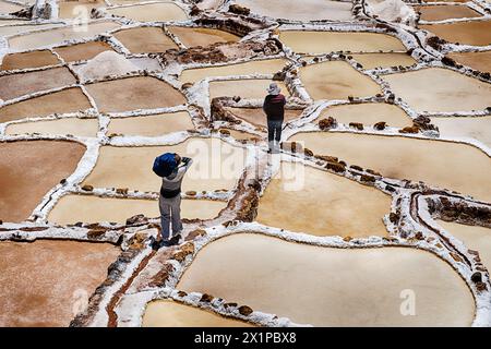 SALINERAS DE MARAS, PERÙ - 2 OTTOBRE 2023: Due operai anonimi percorrono sentieri tra gli stagni salati di evaporazione di Salineras de Maras in Perù Foto Stock