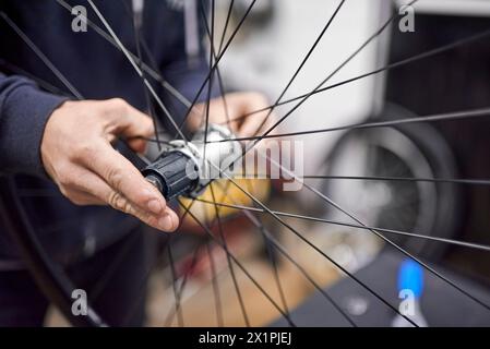 Uomo irriconoscibile che monta un assale ruota per bici dopo averlo smontato per la pulizia e l'ingrassaggio nell'ambito di un servizio di manutenzione per biciclette. Persone vere Foto Stock