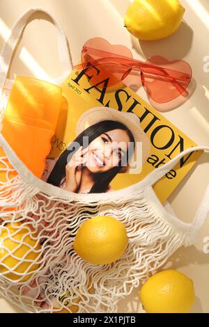 Borsa a corde con limoni freschi, rivista di moda e accessori da spiaggia su sfondo beige, piatto Foto Stock