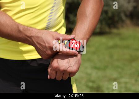 Uomo che utilizza la funzione SOS su uno smartwatch all'aperto, primo piano Foto Stock