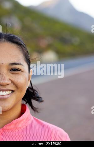 Una donna birazziale che indossa una cima rosa sorride all'aperto in mezzo alla natura, spazio copia Foto Stock