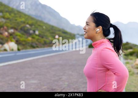 Una donna birazziale che indossa una cima rosa in piedi su una strada, circondata dalla natura, spazio copia Foto Stock