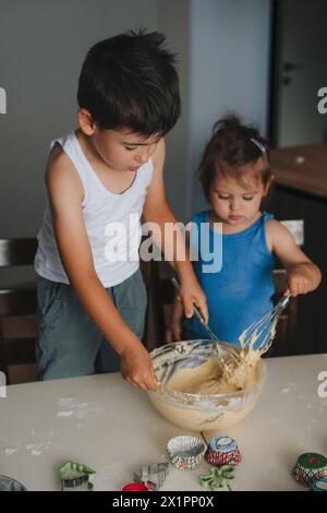 Bambino in età prescolare che mescola l'impasto, ragazza che guarda con interesse per la ciotola. Fratelli che cucinano. Fratello e sorella che fanno sorpresa, aiutano i genitori. Famiglia Foto Stock