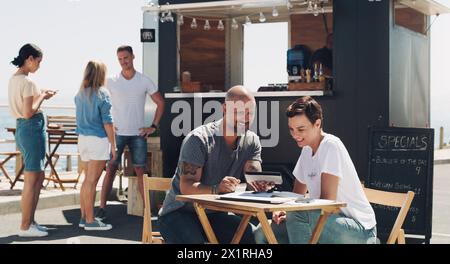 Lavoro di squadra, riunioni e proprietari di piccole e medie imprese con tablet presso il food truck per conversazioni, pianificazione o discussione sul menu. Ristorante, uomo felice e.. Foto Stock