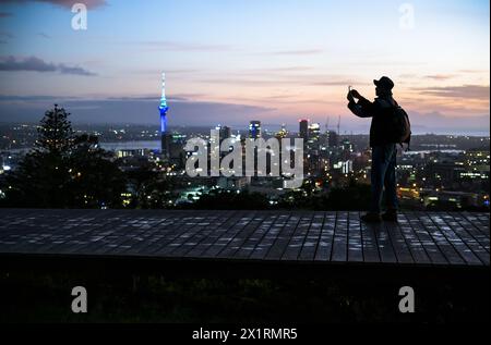 Immagine della silhouette di un turista che scatta foto della Sky Tower e del paesaggio urbano utilizzando lo smartphone. Vetta del Monte Eden all'alba. Auckland. Foto Stock