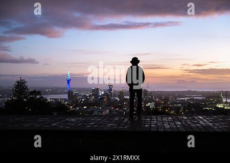 Uomo in silhouette che guarda la vista della Sky Tower e del paesaggio urbano. Vetta del Monte Eden all'alba. Auckland. Foto Stock