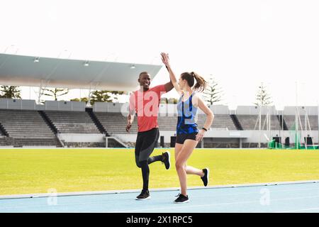 High Five, sport e lavoro di squadra su pista all'aperto, festeggiano e vincono la gara di corsa. Atleti, persone felici e insieme per il fitness a. Foto Stock