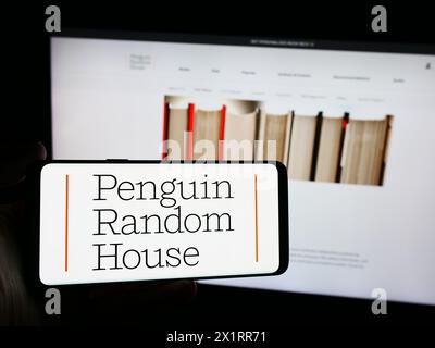 Persona che possiede uno smartphone con il logo della casa editrice statunitense Penguin Random House davanti al sito Web. Mettere a fuoco il display del telefono. Foto Stock