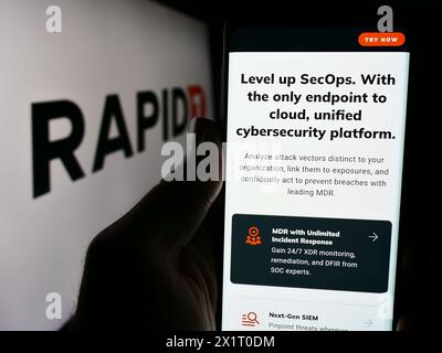 Persona che detiene un cellulare con il sito web della società statunitense di sicurezza informatica Rapid7 davanti al logo aziendale. Messa a fuoco al centro del display del telefono. Foto Stock