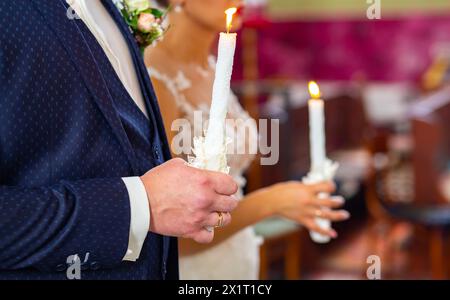 Sposa e sposo in corone dorate in piedi con candele in mano durante la cerimonia nuziale. Coppia spirituale. Matrimonio in chiesa. roma emotiva Foto Stock