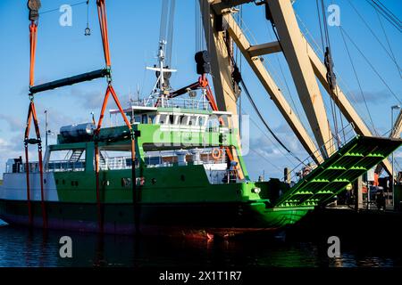 Neuharlingersiel, Germania. 18 aprile 2024. La gru galleggiante 'Enak' solleva il traghetto 'Spiekeroog IV' nel bacino del porto. La nave da 300 tonnellate, utilizzata per i servizi di traghetto per l'isola della Frisona orientale di Spiekeroog, si era allontanata dal suo ormeggio durante la tempesta "Zoltan" nel dicembre 2023 e su un'area di parcheggio nel porto. Crediti: Hauke-Christian Dittrich/dpa/Alamy Live News Foto Stock