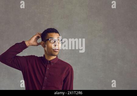 Interrogare un uomo afroamericano che gratta la testa in piedi su uno spazio di copia grigio Foto Stock