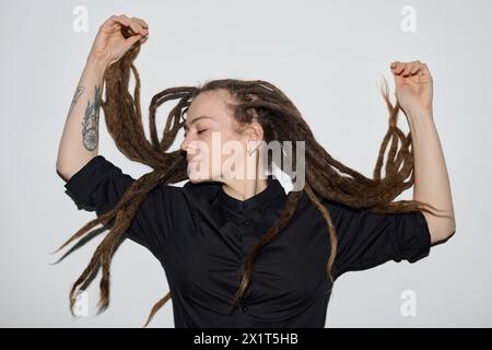 Ritratto minimale di donna caucasica con lunghi dreadlock che ballano su sfondo bianco scattato con flash Foto Stock