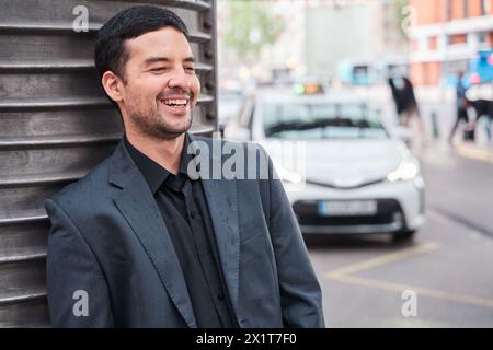 allegro latino in blazer che ride mentre viene sostenuto e aspetta Foto Stock