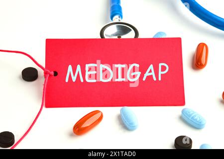 Concetto medico. MEDIGAP su scheda rossa su sfondo bianco, accanto a uno stetoscopio e pillole, vitamine Foto Stock