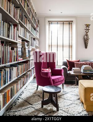 Poltrona wingback rivestita rosa con ripiani di libri a Chelsea home, Londra, Regno Unito Foto Stock