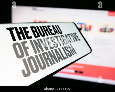 Smartphone con logo dell'organizzazione il Bureau of Investigative Journalism (TBIJ) di fronte al sito Web. Mettere a fuoco la parte centrale sinistra del display del telefono. Foto Stock