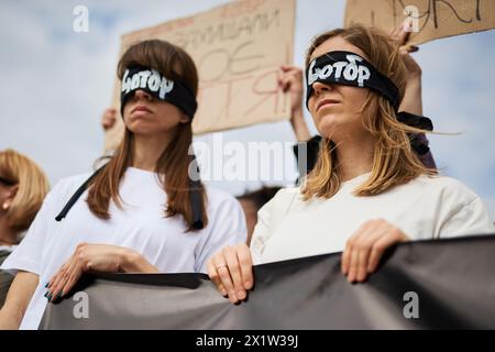 Due donne ucraine con gli occhi legati giocano le persone catturate che rimangono nelle prigioni russe e non riescono a vedere il mondo libero. Kiev - 13 aprile 2024 Foto Stock