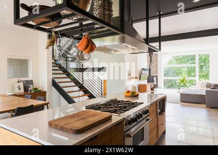 Isola americana in legno di noce con ripiano in quarzite e piano cottura a gas incorporato in cucina all'interno di una casa in stile cubo moderno, Quebec, Canada Foto Stock