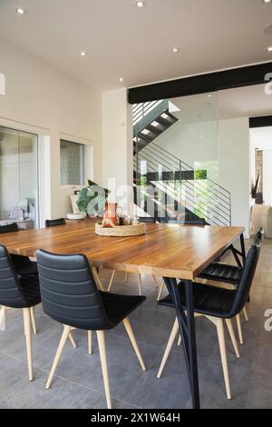 Tavolo da pranzo in legno di noce americano e poltrone in pelle nera con gambe in legno di frassino nella sala da pranzo all'interno di una casa in stile cubo moderno, Quebec, Canada Foto Stock