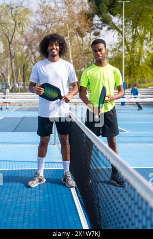 Ritratto verticale di due giovani giocatori afroamericani di pallacanestro in piedi che guardano la macchina fotografica che regge l'attrezzatura da pallacanestro Foto Stock