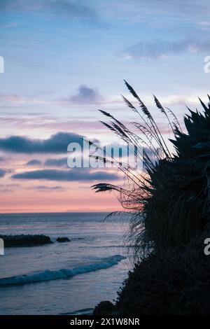 Un bellissimo tramonto sull'oceano con una spiaggia sullo sfondo. Il cielo è pieno di nuvole e l'acqua è calma Foto Stock