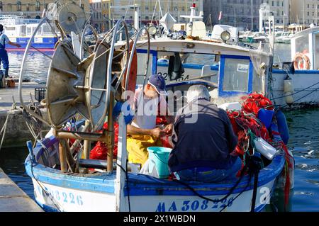 Un pescatore ripara le reti sulla sua barca blu nel porto tranquillo durante il giorno, Marsiglia, dipartimento Bouches-du-Rhone, Provence-Alpes-Cote Foto Stock