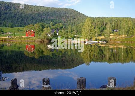 Alberi, case e una piccola barca si riflettono in un lago calmo, un vecchio canale navigabile, Telemark Canal, Telemark, Norvegia Foto Stock