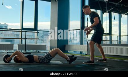 Donna caucasica atleta ragazza che si allena con uomo allenatore allenatore di sport personale in palestra lancio passare indietro medicina palla atletica coppia allenamento in Foto Stock