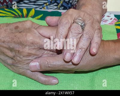 Su un tavolo, con una tovaglia verde, madre e figlio si tengono per mano. Lei, con le mani invecchiate e stropicciate dal tempo, con un anello al dito, la tiene così Foto Stock