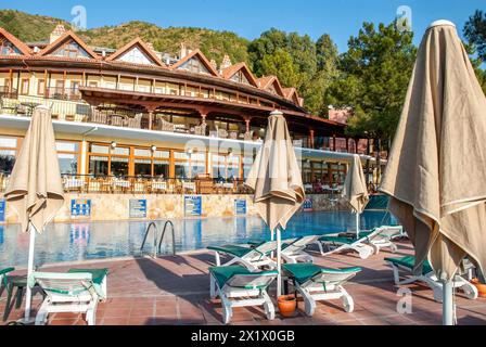 Resort sul mare con una splendida piscina e comode poltrone con ombrelloni ripiegati la mattina presto Foto Stock