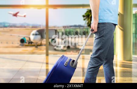 Foto di un giovane che cammina con i suoi bagagli attraverso la sala partenze di un aeroporto Foto Stock