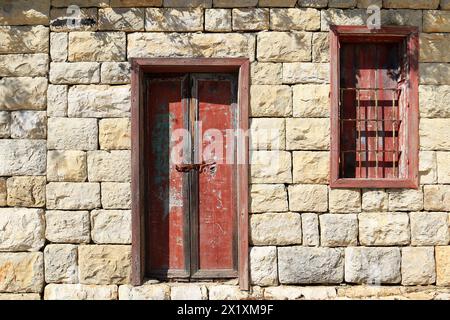 Una porta e una finestra chiuse in legno con vernice rossa sbucciata. Foto Stock