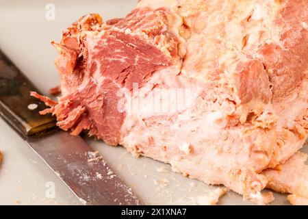 Il prosciutto affettato poggia su un tagliere accanto a un coltello da intaglio, parzialmente intagliato con carne succulenta visibile, indicativo della preparazione dei pasti per un'andatura festosa Foto Stock