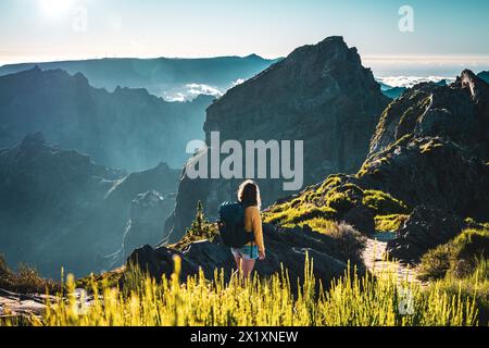 Descrizione: Il turista cammina lungo un sentiero panoramico e si affaccia sulle profondità mozzafiato di una valle ricoperta di nuvole in una montagna vulcanica Foto Stock