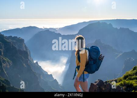 Descrizione: Backpacker toruist si trova sul bordo ventoso di una valle profonda e ricoperta di nuvole e gode di una vista panoramica mozzafiato sulla montagna vulcanica Foto Stock