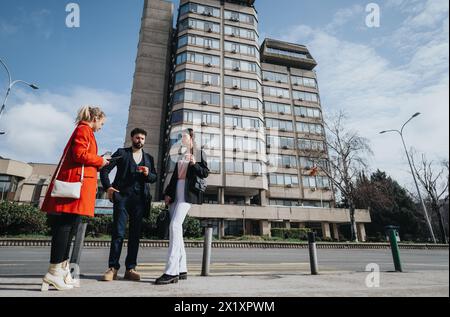 Tre giovani professionisti impegnati in una riunione informale all'aperto in città con un edificio per uffici sullo sfondo Foto Stock