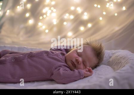 Bimba appena nata che dorme in una stanza buia con luci fiabesche sullo sfondo Foto Stock