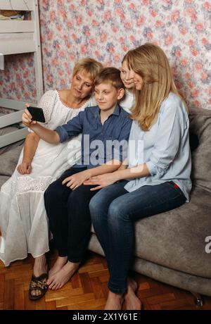 Una donna e due bambini sono seduti su un divano in un soggiorno, impegnati in una conversazione e trascorrendo del tempo insieme. Foto Stock