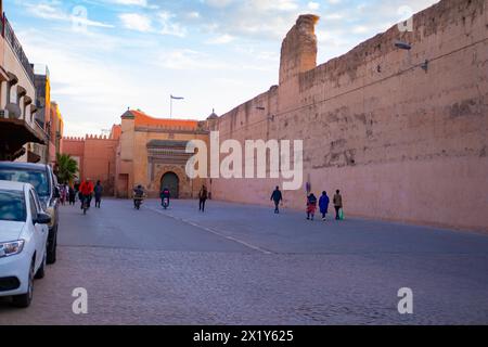 La gente cammina lungo l'alto muro della città Rossa di Marrakech affrettati a dedicarsi agli affari, all'autentico paesaggio urbano africano, alle attività quotidiane e alle interazioni che la gente vive Foto Stock