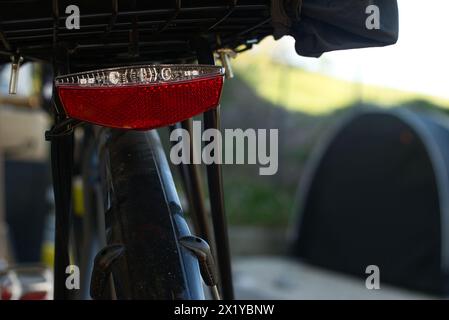 Vista ravvicinata di una luce di coda rossa e bianca montata su una bicicletta con portabagagli. Sullo sfondo, una tenda nera è sfocata. La scena sei tu Foto Stock