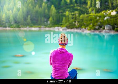 Descrizione: La donna siede su una grande roccia e gode del sole e della vista sul bellissimo lago turchese Sorapis nel pomeriggio. Lago Sorapis, Dolomiti, bel Foto Stock