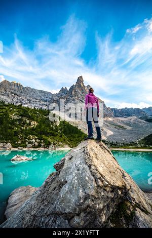 Descrizione: Donna atletica in piedi su un grande masso al turchese lago di Sorapis con dito di dio sullo sfondo la sera. Lago Sorapis, Dolomiti Foto Stock