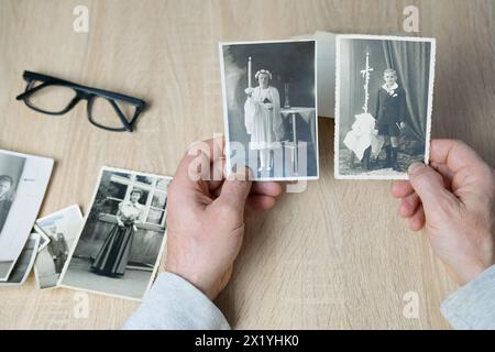 uomo che tiene in mano vecchie fotografie monocromatiche d'epoca di bambini 1940 - 1950 in colore seppia sono sparse su un tavolo di legno, concetto di genealogia, memor Foto Stock