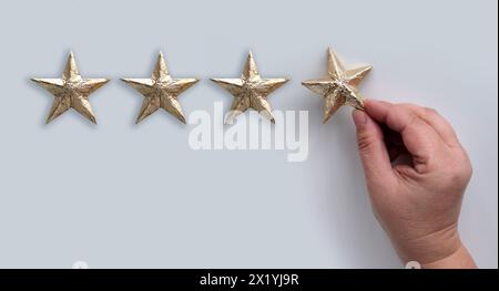 Mano femminile con una stella laminata d'oro su sfondo bianco, il concetto di valutare il risultato, la valutazione, la soddisfazione Foto Stock