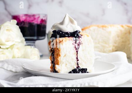 Torta Angel Food con salsa ai mirtilli e panna montata: Fetta di torta di pan di Spagna con marmellata di mirtilli e crema chantilly su un piatto Foto Stock