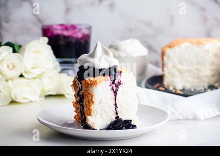 Torta Angel Food con salsa ai mirtilli e panna montata: Fetta di torta di pan di Spagna con marmellata di mirtilli e crema chantilly su un piatto Foto Stock