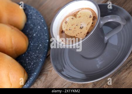 Caffè cappuccino in tazza grigia e piattino su un vecchio tavolo di legno, schiuma a forma di cuore, croissant freschi ruvidi, pasticceria fresca di concetto, caffè mattutino, ca Foto Stock